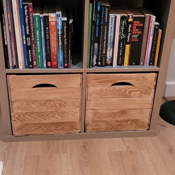 Wooden crates with handles in the bottom row of a shelf, above a compartment with books